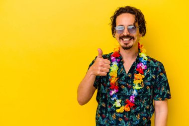 Sarı arka planda izole edilmiş Hawaii kolyesi takan beyaz bir adam gülümsüyor ve başparmağını kaldırıyor.