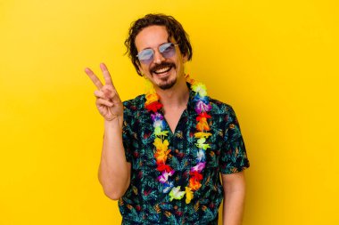 Sarı arka planda izole edilmiş beyaz bir kolye takan genç beyaz adam neşeli ve kaygısız parmakları olan bir barış sembolü gösteriyor..