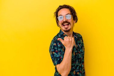 Sarı arka plan noktalarında izole edilmiş yaz kıyafetleri giyen genç beyaz adam başparmak uzakta, gülüyor ve kaygısız..