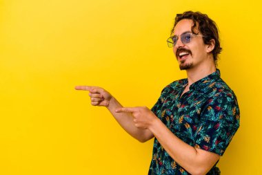 Sarı arka planda izole edilmiş yaz kıyafetleri giyen genç beyaz adam işaret parmağıyla işaret ederek heyecanlanıyor..