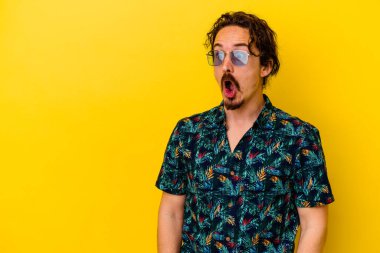 Sarı arka planda izole edilmiş yaz kıyafetleri giyen genç beyaz adam gördüğü bir şey yüzünden şoka uğruyor..