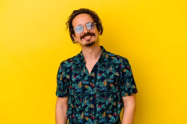 Sarı arka planda izole edilmiş yaz kıyafetleri giyen genç beyaz adam mutlu, güler yüzlü ve neşeli..