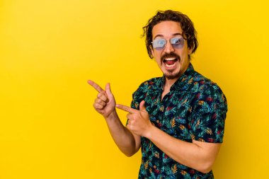 Sarı arka planda izole edilmiş yaz kıyafetleri giyen genç beyaz bir adam işaret parmağıyla fotokopi alanını işaret ederek heyecan ve arzusunu ifade ediyor..