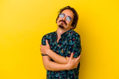 Sarı arka plan kucaklamalarında izole edilmiş yaz kıyafetleri giyen genç beyaz adam, kaygısızca gülümsüyor ve mutlu..
