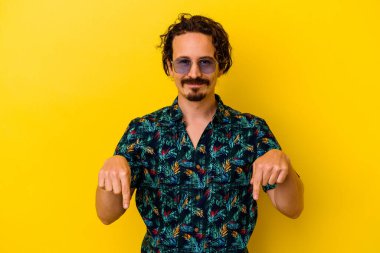 Sarı arka planda izole edilmiş yaz kıyafetleri giyen genç beyaz adam parmaklarıyla aşağıya doğru, olumlu bir his..