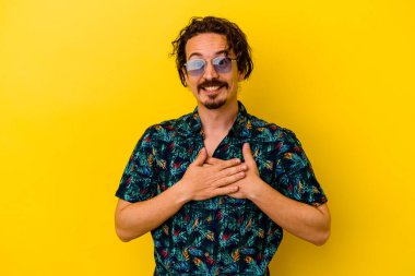 Sarı arka planda izole edilmiş yaz kıyafetleri giyen beyaz bir genç, dost bir ifadeye sahip, avuçlarını göğsüne bastırıyor. Aşk konsepti.