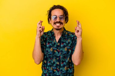 Sarı arka planda izole edilmiş yaz kıyafetleri giyen beyaz bir adam şans getirsin diye dua ediyor.