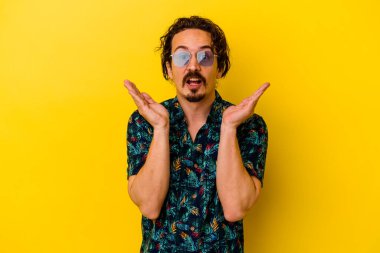 Sarı arka planda izole edilmiş yaz kıyafetleri giyen genç beyaz adam şaşırdı ve şok oldu..