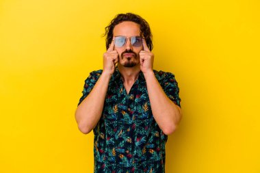 Sarı arka planda izole edilmiş yaz kıyafetleri giyen genç beyaz adam bir işe odaklanmış, işaret parmaklarını işaret ediyor..