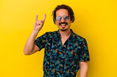 Sarı arka planda izole edilmiş yaz kıyafetleri giyen genç beyaz bir adam devrim konsepti olarak boynuzlarını gösteriyor..