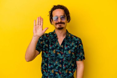 Sarı arka planda izole edilmiş yaz kıyafetleri giyen genç beyaz adam gülümseyerek beş numarayı parmaklarıyla gösteriyor..