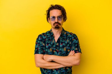 Sarı arka planda izole edilmiş yaz kıyafetleri giyen genç beyaz adam alaycı bir ifadeyle kameraya bakıyor..