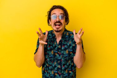 Sarı arka planda izole edilmiş yaz kıyafetleri giyen genç beyaz bir adam zaferi ya da başarıyı kutluyor, şaşırıyor ve şok oluyor..