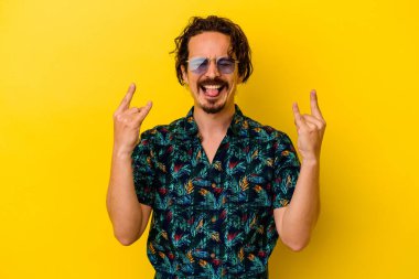 Sarı arka planda izole edilmiş yaz kıyafetleri giyen genç beyaz adam parmaklarıyla taş hareketi gösteriyor.