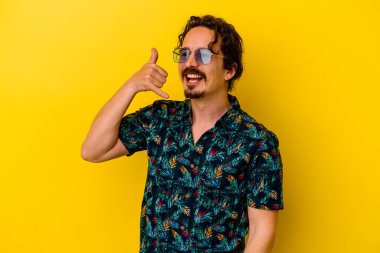 Sarı arka planda izole edilmiş yaz kıyafetleri giyen genç beyaz adam parmakları olan bir cep telefonu hareketi gösteriyor..