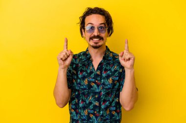 Sarı arka planda izole edilmiş yaz kıyafetleri giyen genç beyaz adam iki ön parmağı da boş bir alan gösteriyor..