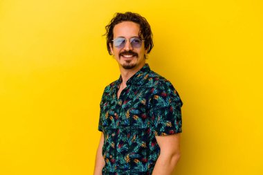 Sarı arka planda izole edilmiş yaz kıyafetleri giyen genç beyaz adam gülümsüyor ve keyifli görünüyor..