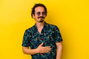 Sarı arka planda izole edilmiş yaz kıyafetleri giyen genç beyaz adam karnına dokunuyor, nazikçe gülümsüyor, yemek yiyor ve tatmin oluyor..