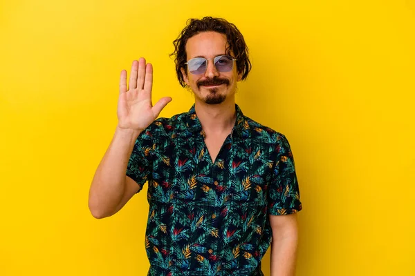 Sarı arka planda izole edilmiş yaz kıyafetleri giyen genç beyaz adam gülümseyerek beş numarayı parmaklarıyla gösteriyor..