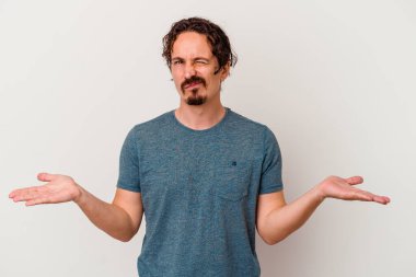 Beyaz arka planda izole edilmiş genç beyaz bir adam sorgulama sırasında omuz silkiyor ve şüphe duyuyor..