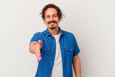 Beyaz arka planda izole edilmiş genç beyaz bir adam selamlama jesti olarak kameraya elini uzatıyor..