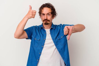 Beyaz arka planda izole edilmiş genç beyaz bir adam baş parmaklarını aşağı ve yukarı kaldırıyor, zor seçim konsepti