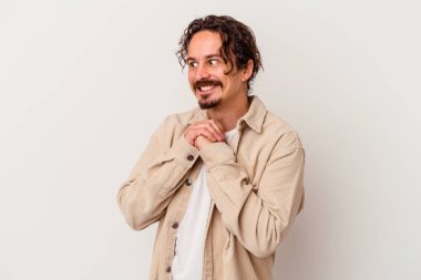 Beyaz arka planda izole genç beyaz adam ellerini çenesinin altında tutuyor, mutlu bir şekilde yana bakıyor..