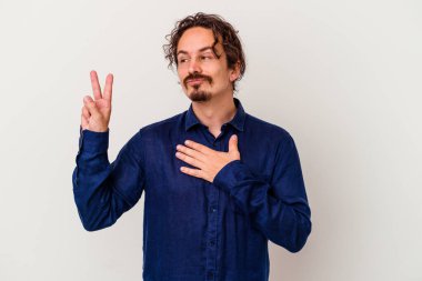 Beyaz arka planda izole edilmiş genç beyaz adam yemin ediyor, elini göğsüne koyuyor..