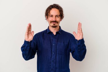 Beyaz arka planda izole edilmiş genç beyaz bir adam işaret parmaklarıyla küçük bir şey tutuyor, gülümsüyor ve kendinden emin..