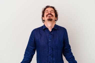 Beyaz arka planda izole edilmiş genç beyaz adam gevşemiş ve mutlu bir şekilde gülüyor, boynunda dişlerini gösteriyor..