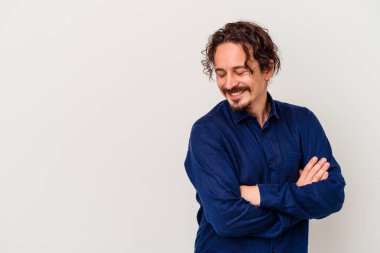 Beyaz arka planda izole edilmiş genç beyaz adam kollarını kavuşturarak gülümsüyor..