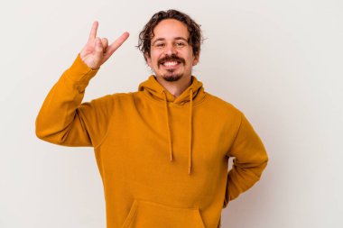 Beyaz arka planda izole edilmiş genç beyaz bir adam parmaklarıyla kaya hareketi gösteriyor.