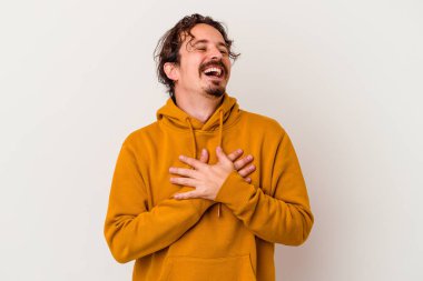 Beyaz arka planda soyutlanmış beyaz tenli genç bir adam gülüyor, elini yüreğine koyuyor, mutluluk kavramını koruyor..