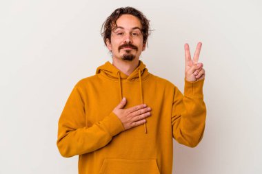 Beyaz arka planda izole edilmiş genç beyaz adam yemin ediyor, elini göğsüne koyuyor..