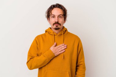 Beyaz arka planda izole edilmiş genç beyaz adam yemin ediyor, elini göğsüne koyuyor..