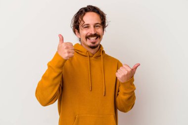 Beyaz arka planda izole edilmiş genç beyaz bir adam iki parmağını da kaldırıyor, gülümsüyor ve kendinden emin..