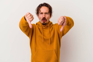 Beyaz arka planda izole edilmiş genç beyaz bir adam baş parmağını aşağı gösteriyor ve hoşlanmadığını ifade ediyor..
