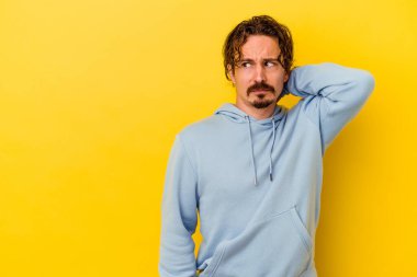 Kafkasyalı genç adam sarı arka planda izole edilmiş kafasının arkasına dokunuyor, düşünüyor ve bir seçim yapıyor..