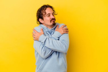 Sarı arka plan kucaklamalarında izole edilmiş genç beyaz adam, kaygısız ve mutlu gülümsüyor..