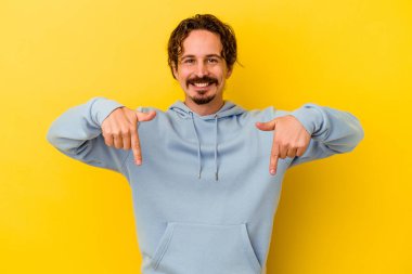 Sarı arka planda izole edilmiş genç beyaz adam parmakları aşağıda, olumlu bir his var..