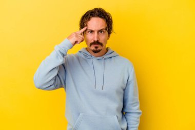 Sarı arka planda izole edilmiş genç beyaz bir adam şakağı parmağıyla işaret ediyor, düşünüyor ve bir göreve odaklanıyor..