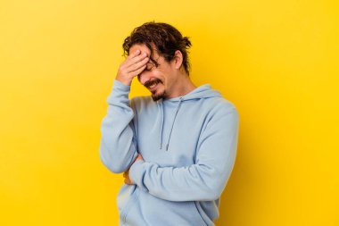 Sarı arka planda izole edilmiş genç beyaz adam kameraya parmaklarıyla göz kırpıyor, yüzünü kapatmaktan utanıyor..