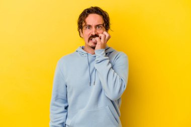 Sarı arka planda izole edilmiş, tırnak yiyen, gergin ve endişeli genç bir beyaz adam..