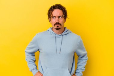 Sarı arka planda izole edilmiş genç beyaz adam şaşkın, şüpheli ve güvensiz hissediyor..