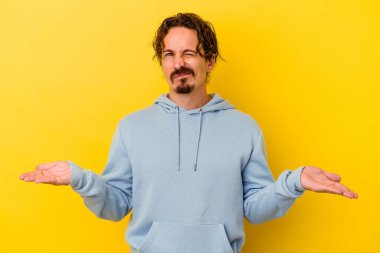 Sarı arka planda izole edilmiş genç beyaz adam sorgulama sırasında omuz silkiyor ve kuşkulanıyor..