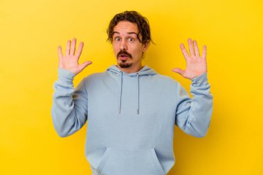 Sarı arka planda izole edilmiş genç beyaz adam gökyüzüne haykırıyor, yukarı bakıyor, hayal kırıklığına uğramış..