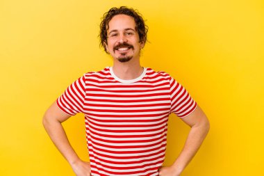 Sarı arka planda izole edilmiş genç beyaz adam ellerini kalçalarına koyuyor..