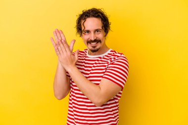 Sarı arka planda izole edilmiş genç beyaz adam enerjik ve rahat hissediyor, ellerini ovuşturuyor kendinden emin..