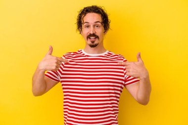 Sarı arka planda izole edilmiş genç beyaz adam parmağını göstererek şaşırdı ve gülümsedi..
