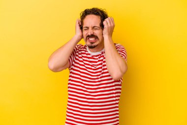Sarı arka planda izole edilmiş genç beyaz adam elleriyle kulakları örtüyor..